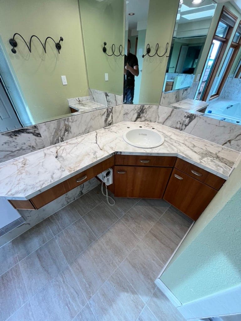 Angled corner vanity with a marble-look porcelain slab counter and backsplash