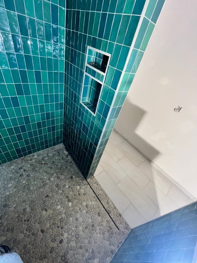 Shower in glossy green square tile with a recessed niche and pebble mosaic floor