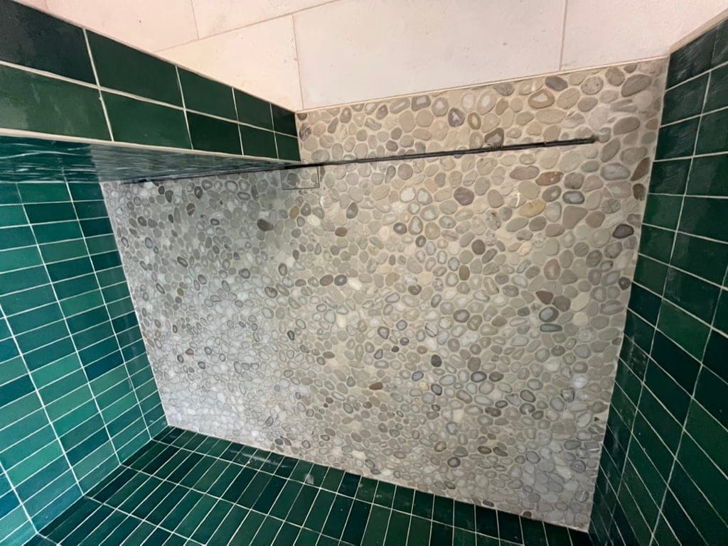 River-pebble mosaic shower floor meeting the green tile curb and walls