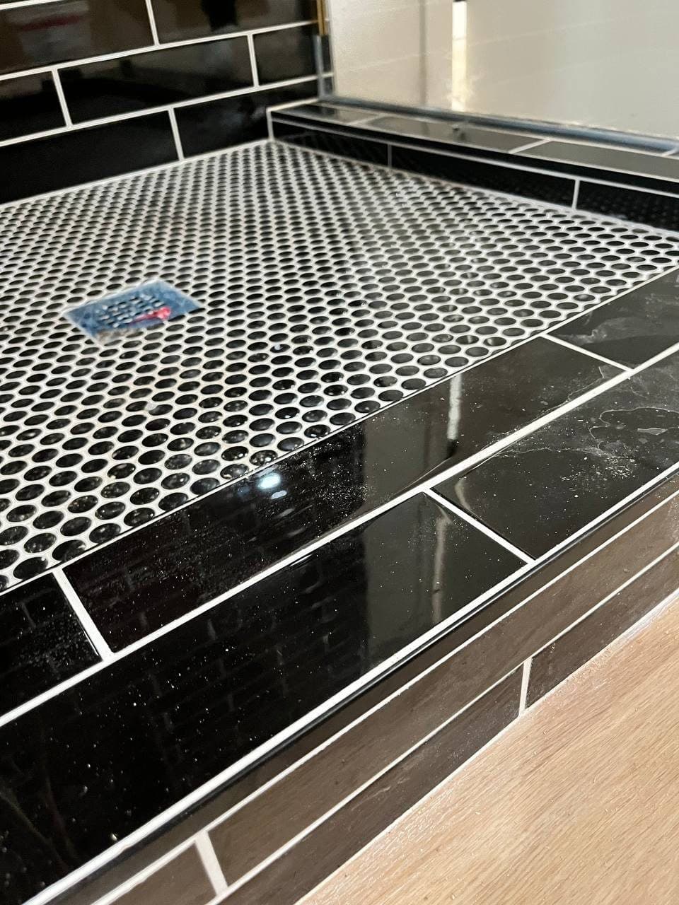 Black penny-round mosaic shower floor next to a wood-look plank bathroom floor