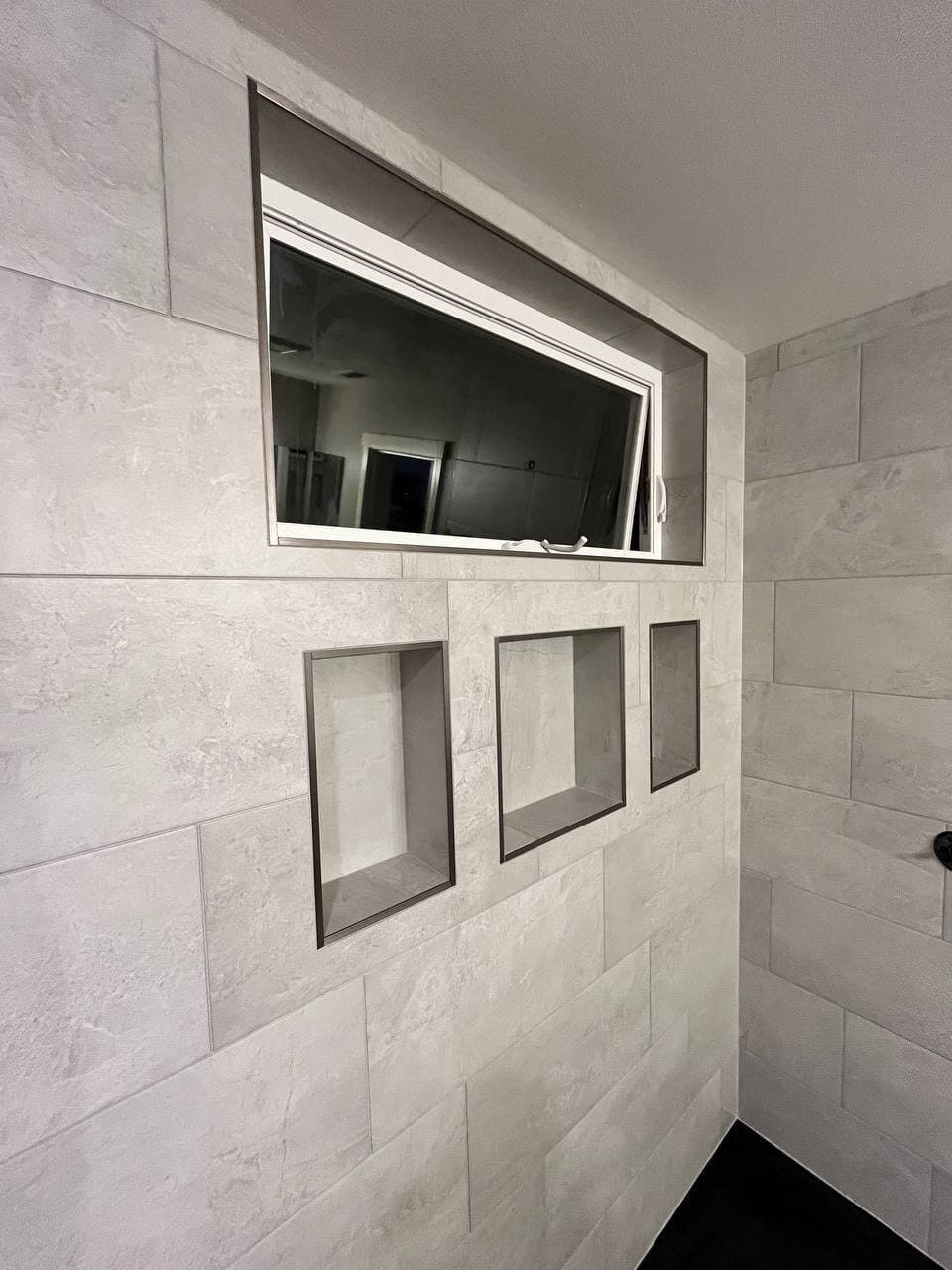 Shower wall in stone-look porcelain with three recessed niches and a tiled window return