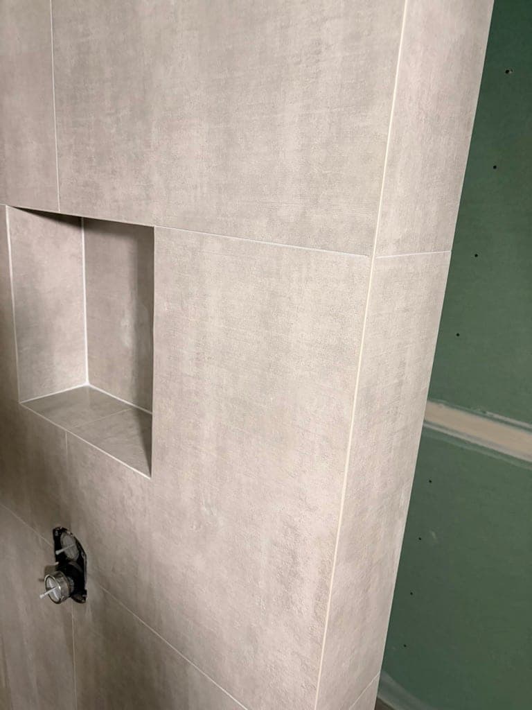 Concrete-look large-format wall tile going up around the shower valve