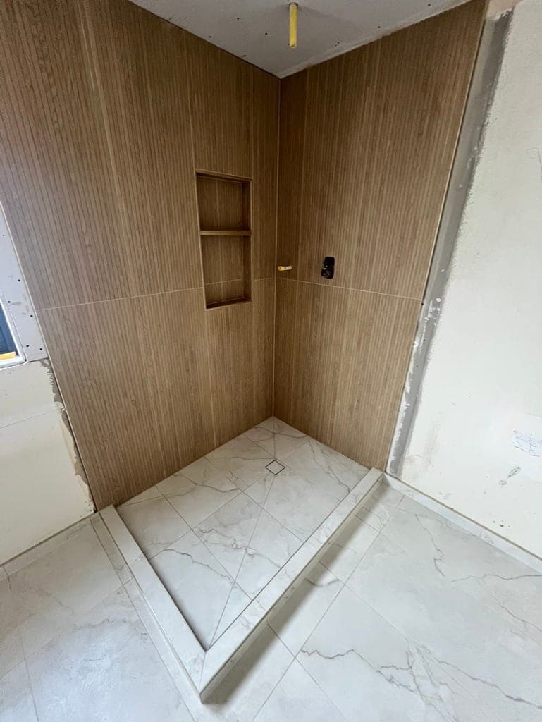 Shower curb and marble-look floor tile set before the glass panel goes in